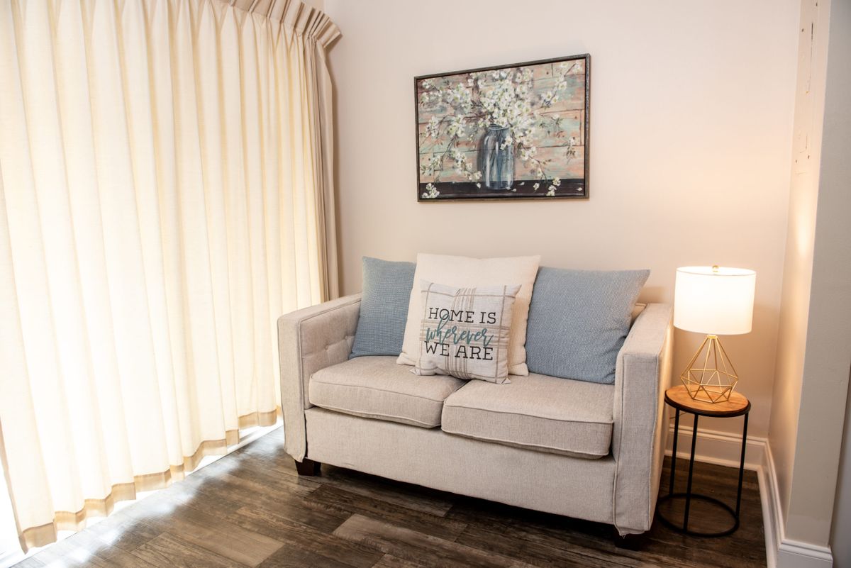 A cozy living room with a beige sofa, decorative cushions, wall art, and soft lighting.