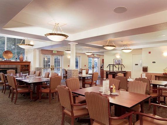 A spacious dining area with neatly arranged tables and chairs, illuminated by stylish ceiling lights.