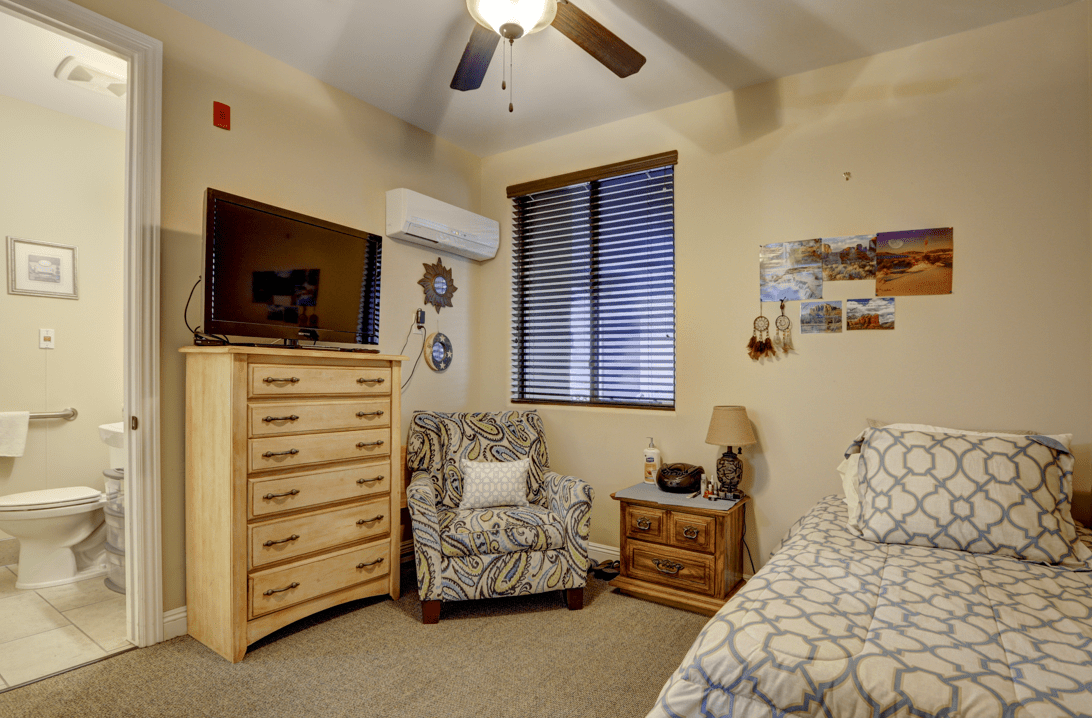 Cozy bedroom with patterned armchair, wooden dresser, and a TV.