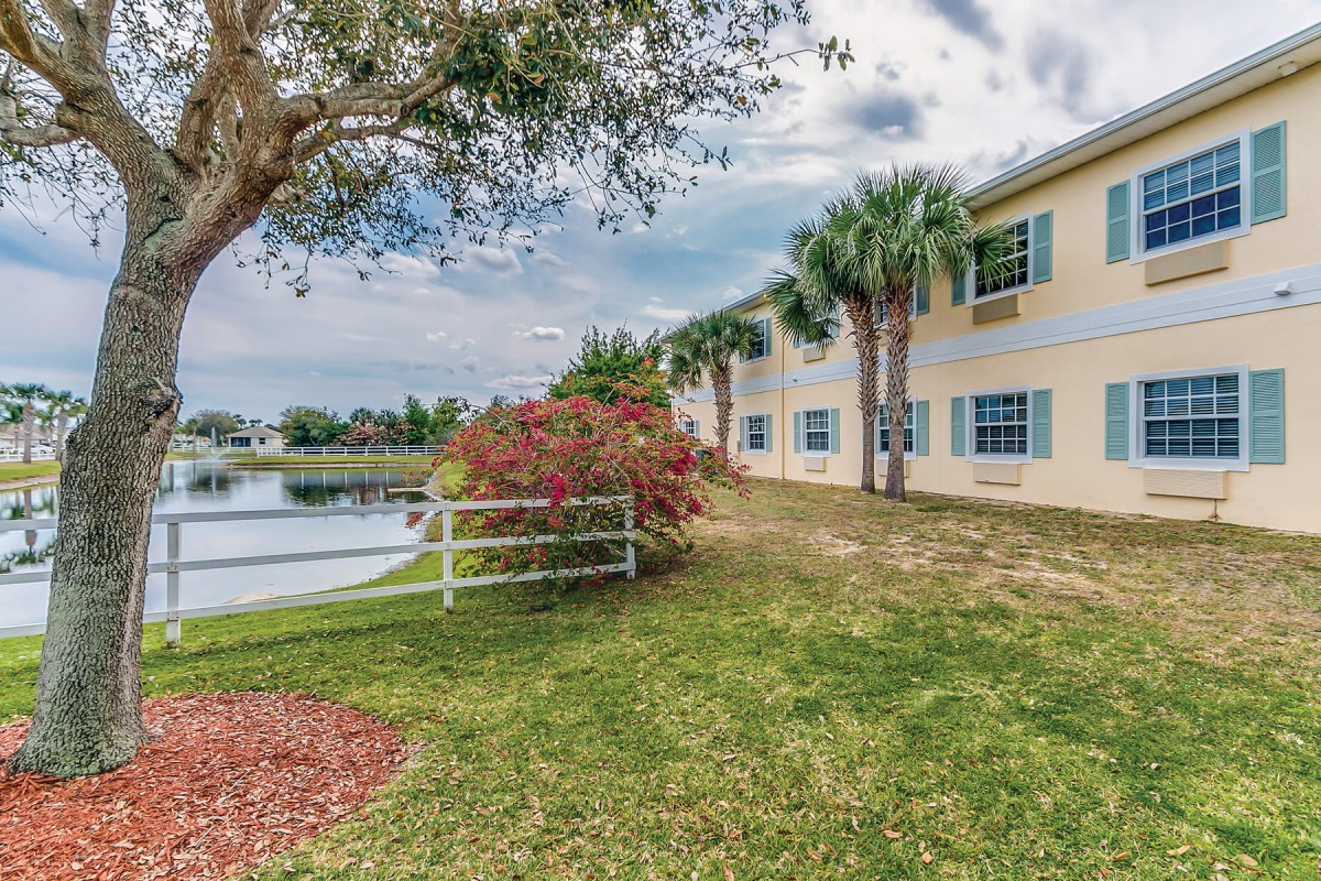 A serene landscape featuring a building by a lake, surrounded by trees and flowers.