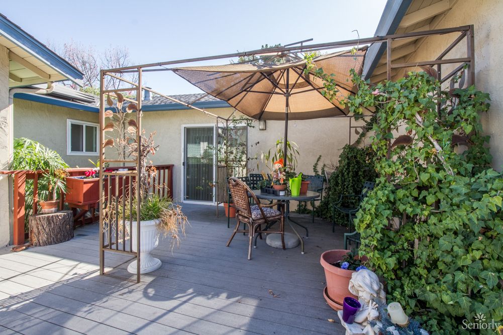 A cozy outdoor patio area with a large umbrella, surrounded by plants and decorative items.