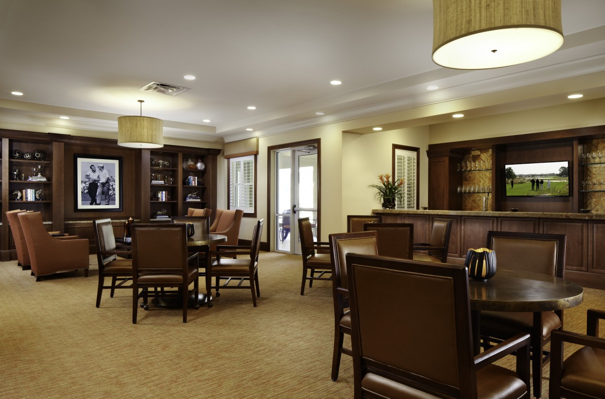 A well-lit dining area featuring several tables and chairs, with elegant lighting and a carpeted floor.
