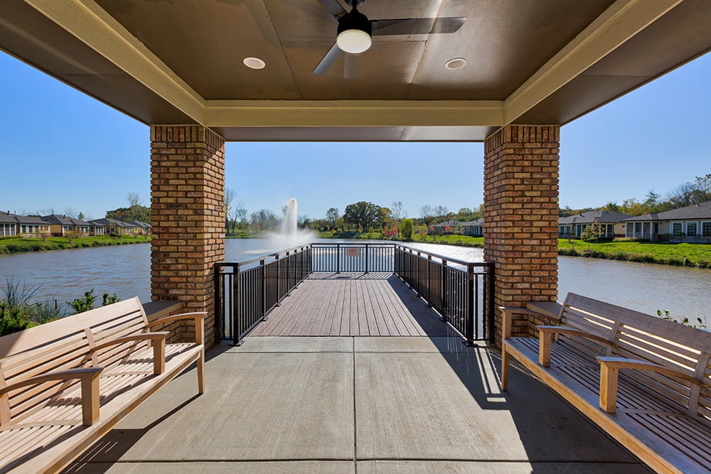 A covered gazebo by the lake with a view of a fountain and ample outdoor seating.