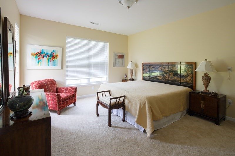 A cozy bedroom with a large bed, upholstered chairs, and vibrant artwork on the walls.