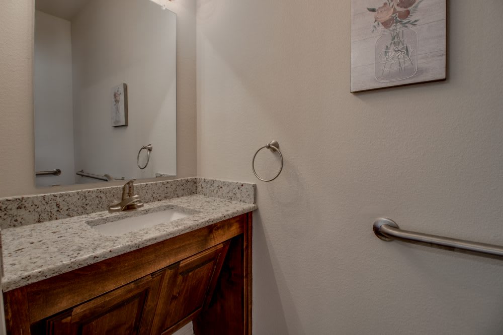 A bathroom with a granite countertop, wooden cabinet, and mirror.