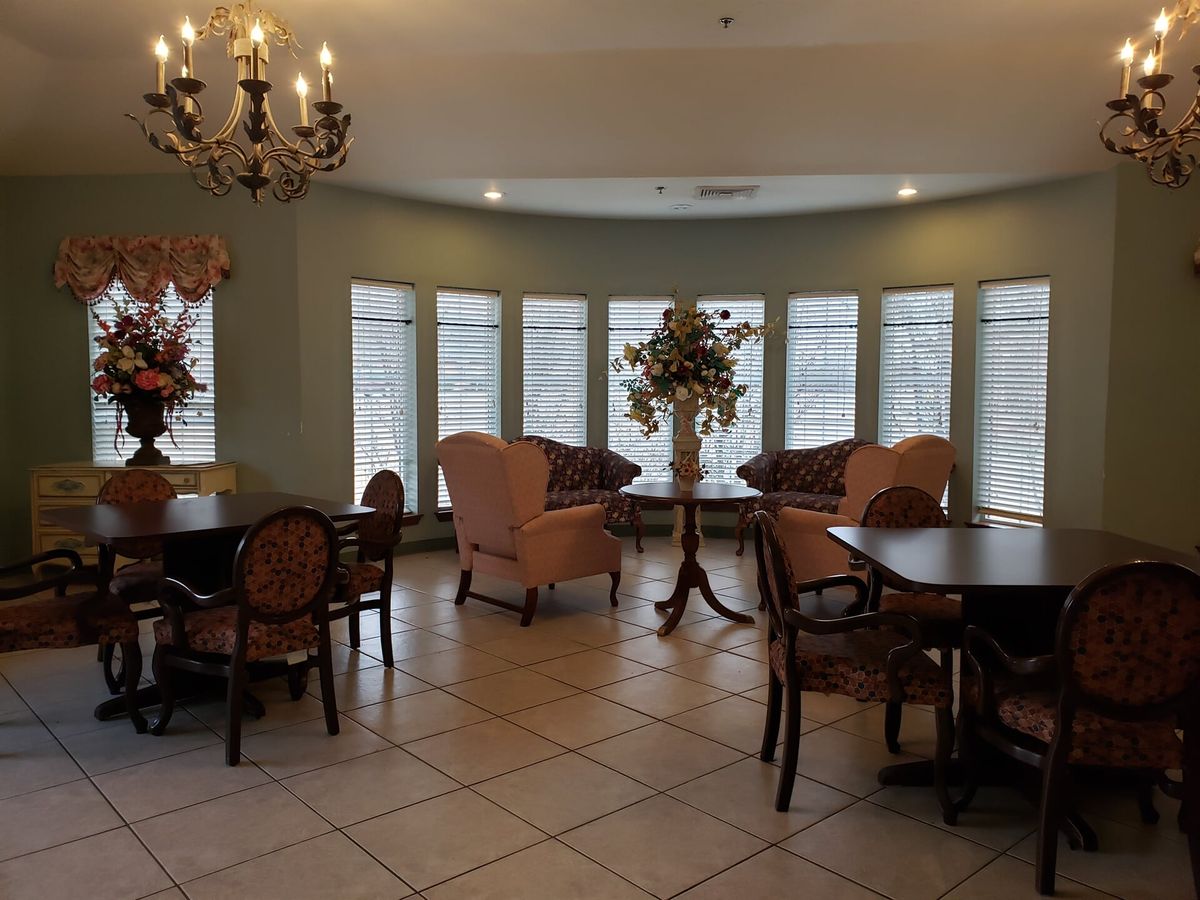 A well-furnished room with tables, chairs, a chandelier, and large windows.