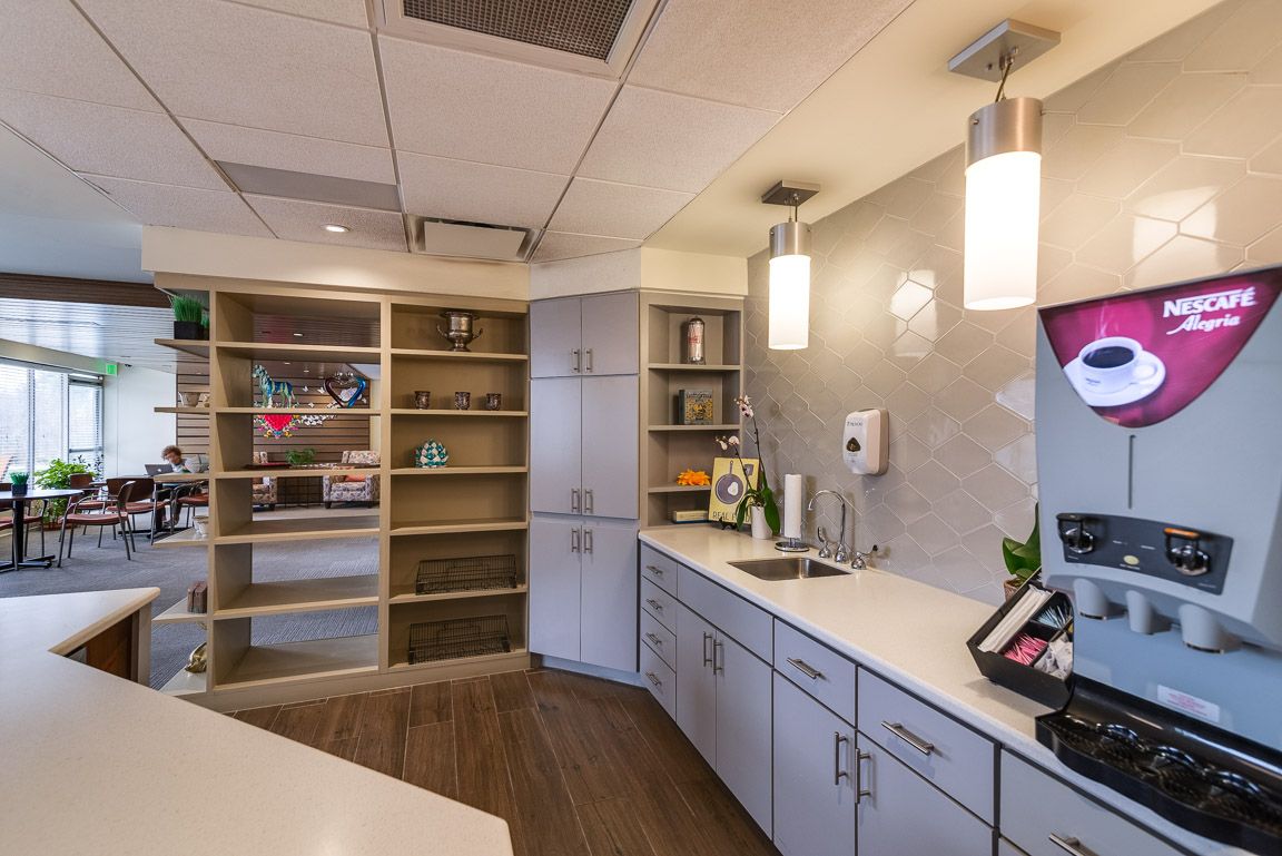 A modern office kitchen with sleek cabinets, open shelving, and pendant lighting.