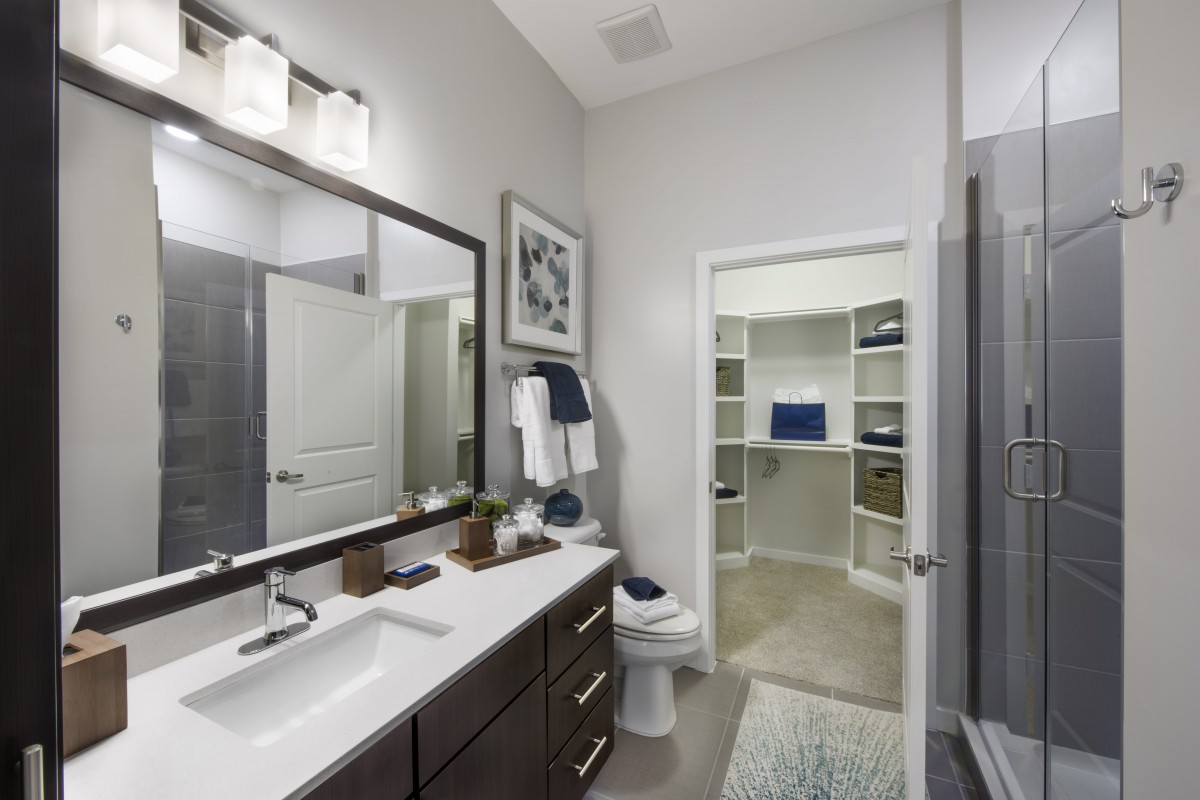 A modern bathroom with a large mirror, sleek cabinetry, and an adjacent walk-in closet.
