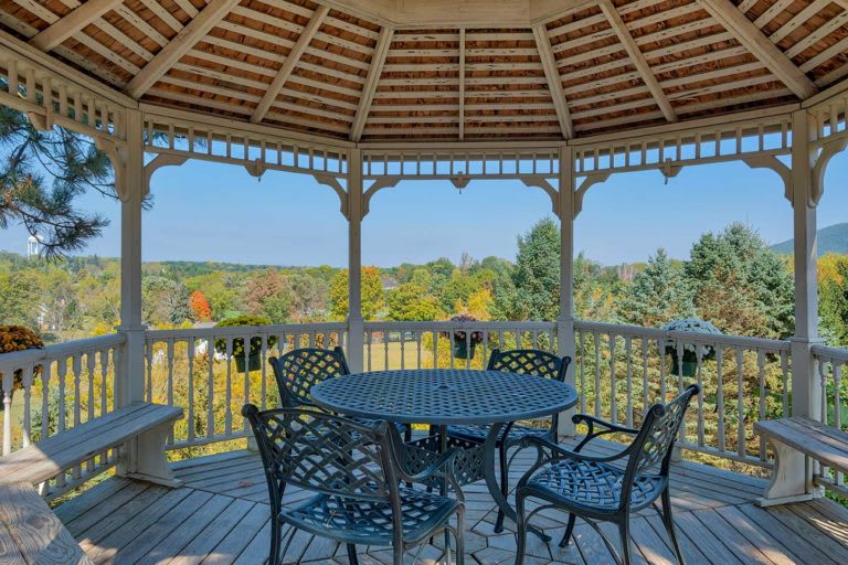 A scenic gazebo with a table and chairs, offering a picturesque view of colorful autumn foliage.