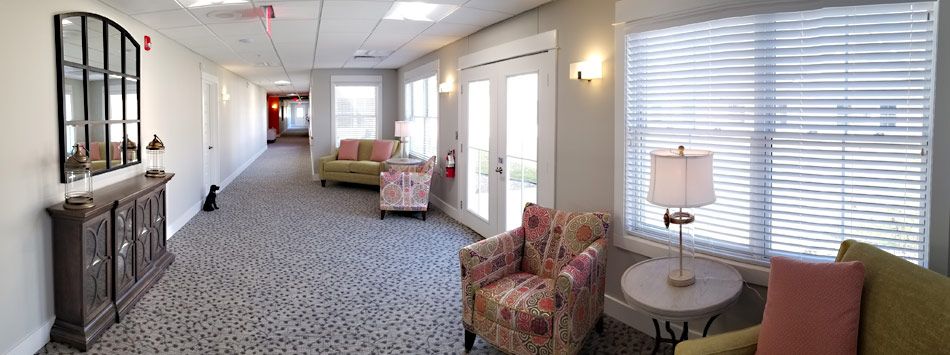 A cozy waiting room with patterned armchairs, a sofa, and large windows letting in natural light.