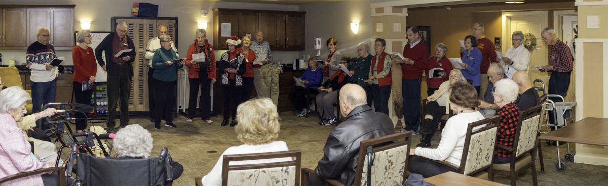 A group of people perform songs for an audience in a community or care facility setting.