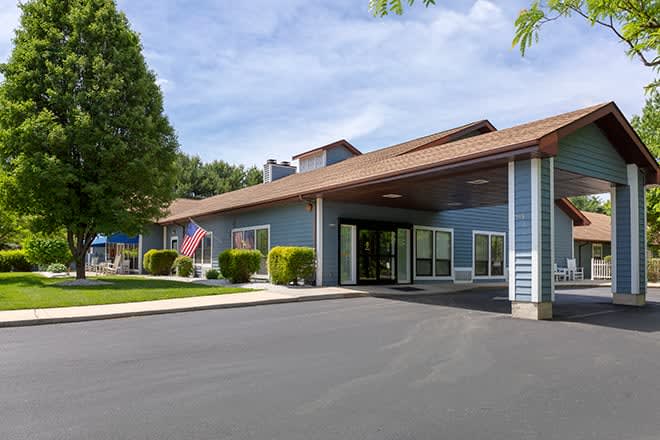 A building with a covered entrance and an American flag, surrounded by trees, under a clear sky.