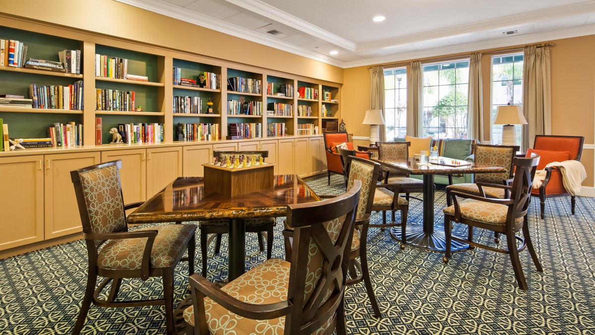 A cozy library room with bookshelves, tables, and chairs arranged for reading.