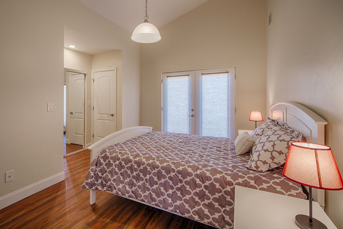 A cozy bedroom featuring a bed with patterned bedding, wooden flooring, and modern lighting.