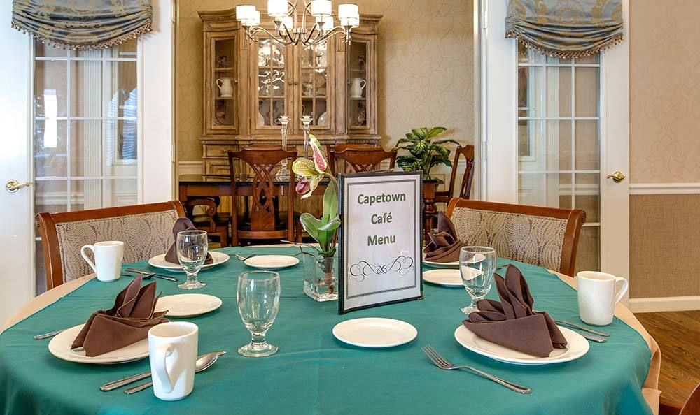 A beautifully set dining table with a teal tablecloth and neatly arranged silverware, featuring a 'Cypress Cafe Menu' sign.