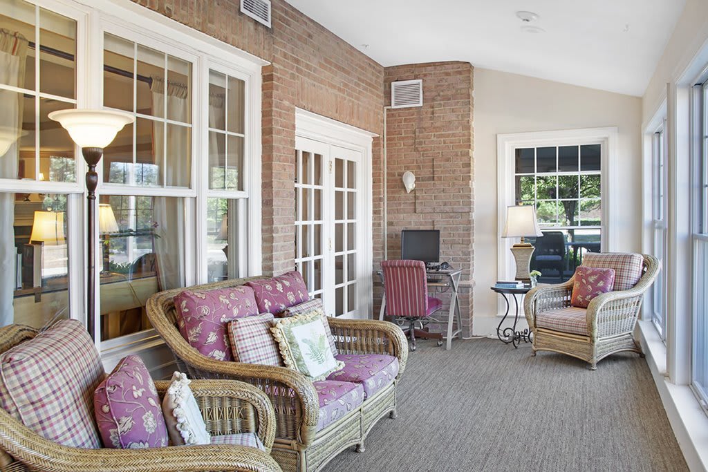 A cozy sunroom featuring wicker furniture, large windows, and a carpeted floor.