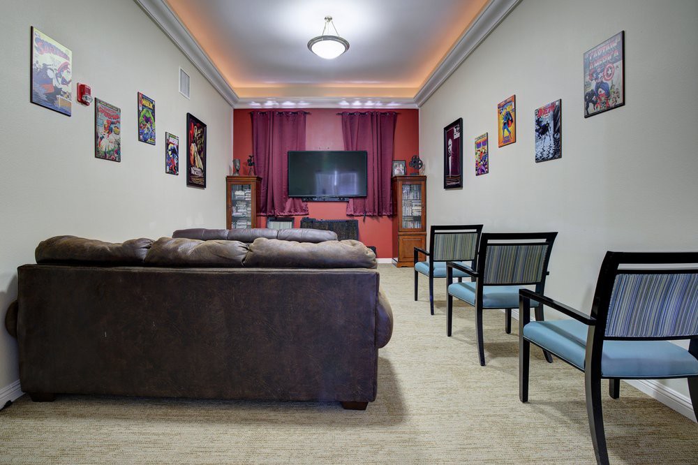 A cozy home theater setup with a sofa and chairs facing a television, surrounded by movie posters on the walls.