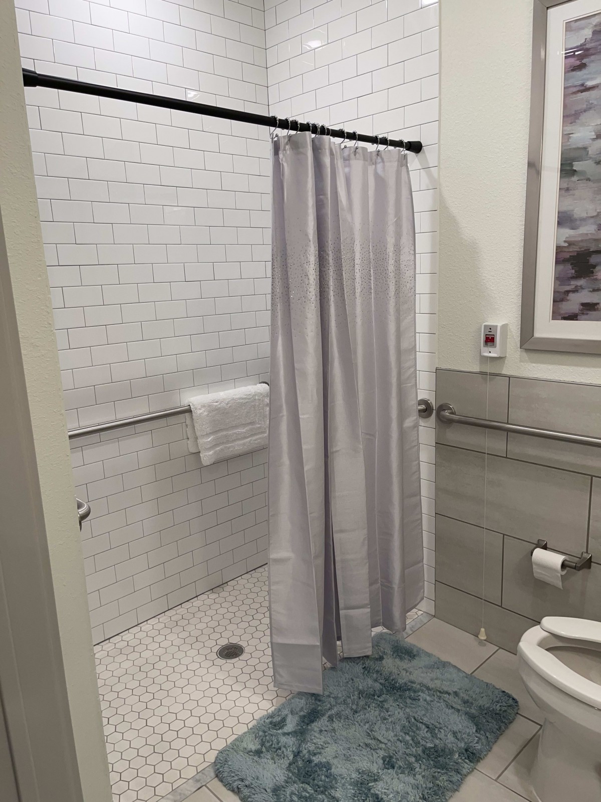 A modern bathroom with a shower, white tiles, and a blue bath mat.