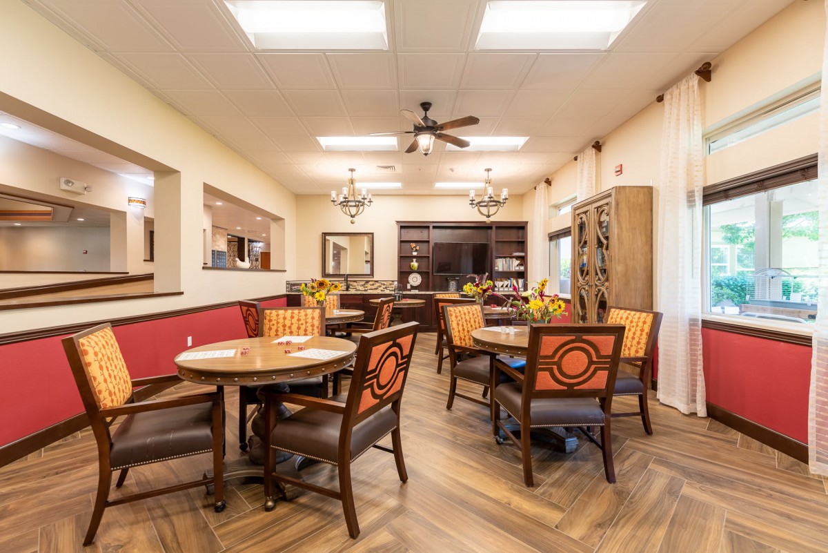 A well-lit dining area with wooden tables, upholstered chairs, and a ceiling fan.