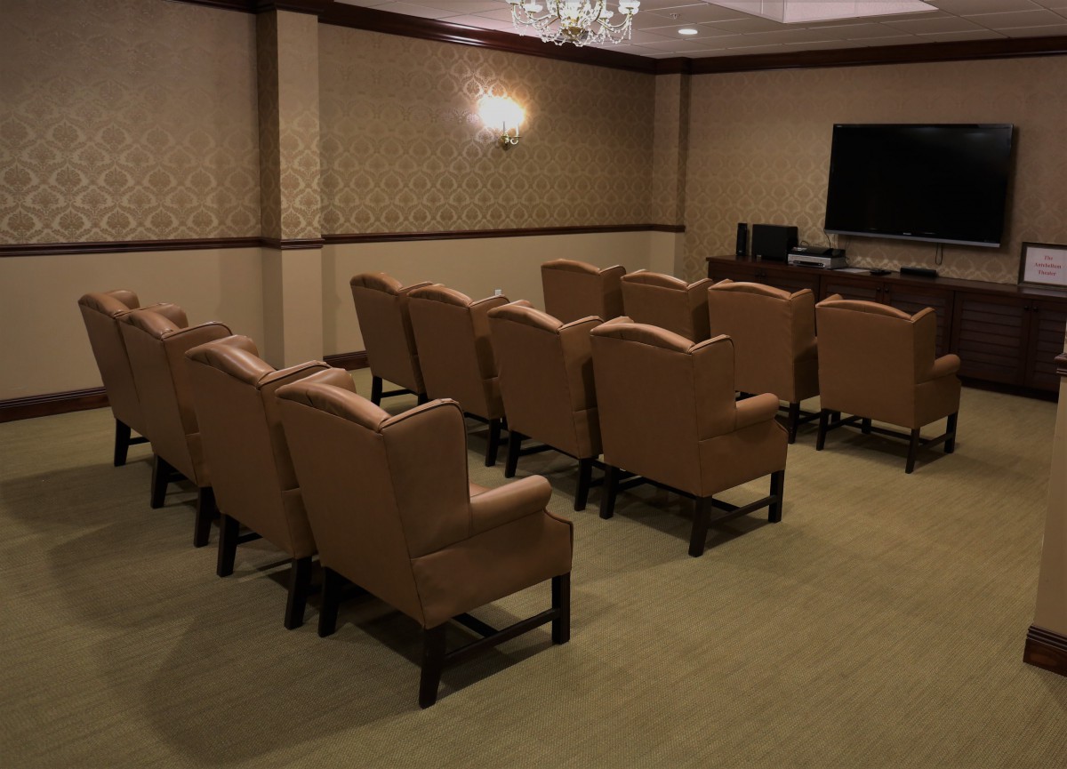 A small conference room with multiple rows of upholstered chairs facing a television screen.