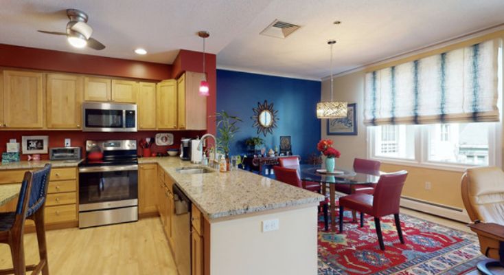 A modern kitchen and dining area with an open concept design featuring a spacious island, stainless steel appliances, and vibrant color accents.