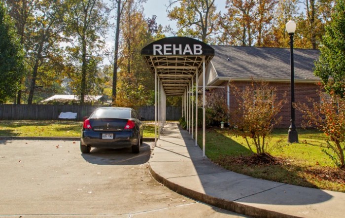 The entrance to a rehab facility with a car parked in front, featuring an awning labeled 'REHAB'.