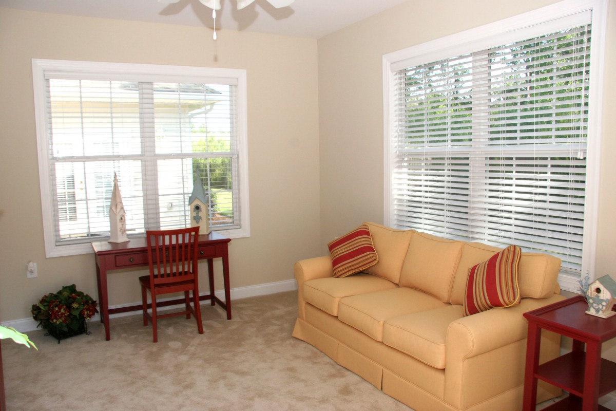 A cozy living room with a yellow sofa, desk, and chair by the window.