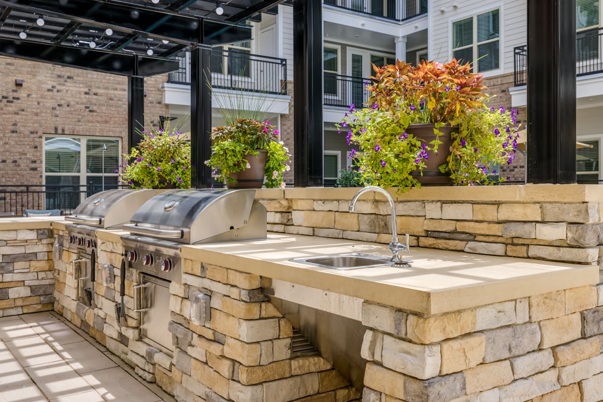 A modern outdoor kitchen area with a grill and sink, adorned with vibrant potted plants under a pergola.