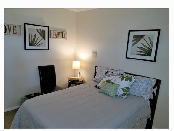 A cozy bedroom with simple decor, featuring a neatly made bed, a bedside lamp, and framed leaf artwork on the walls.