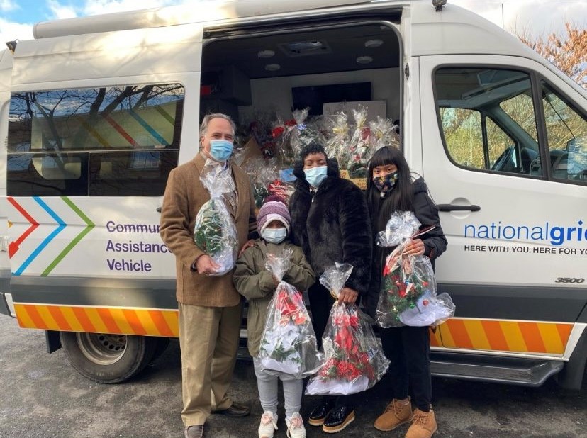 A group of people standing in front of a van, holding gift baskets while dressed in winter clothing and face masks.