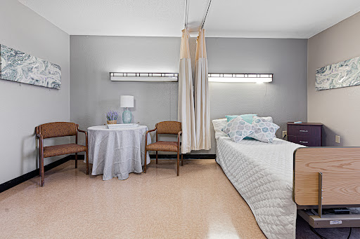 A serene hospital room featuring a bed, chairs, and a small table, designed for patient comfort.