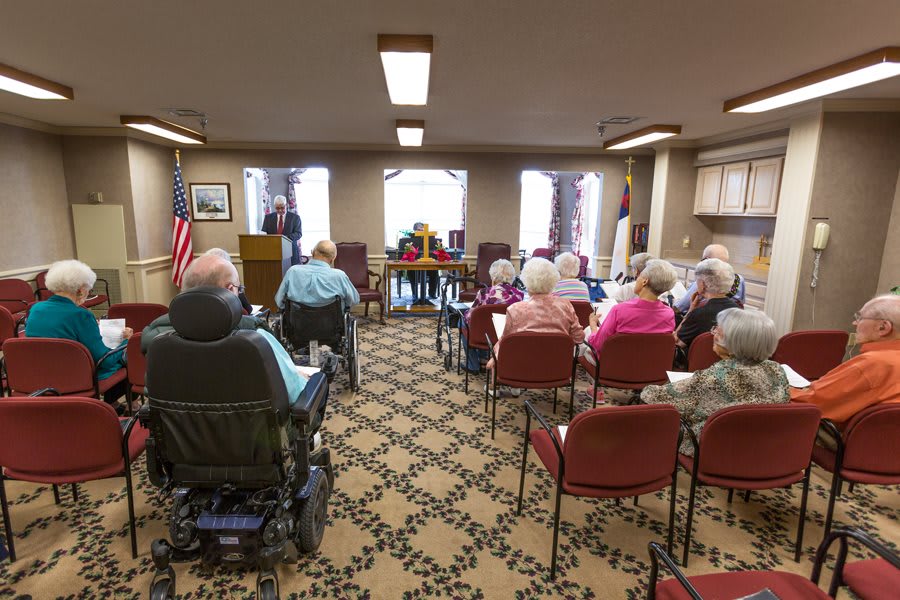 A group of senior individuals attending a meeting in a community center room.