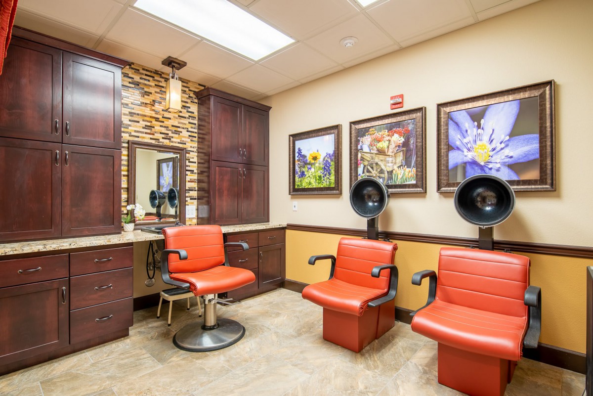A modern salon interior featuring red chairs, hair dryers, and wall art.