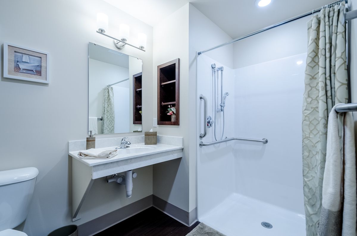A modern and clean bathroom with a sink, large mirror, and walk-in shower.