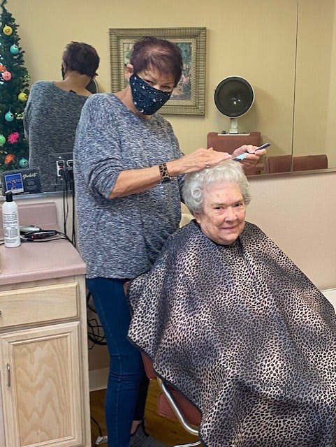 A senior woman gets her hair styled by a masked hairdresser in a salon.