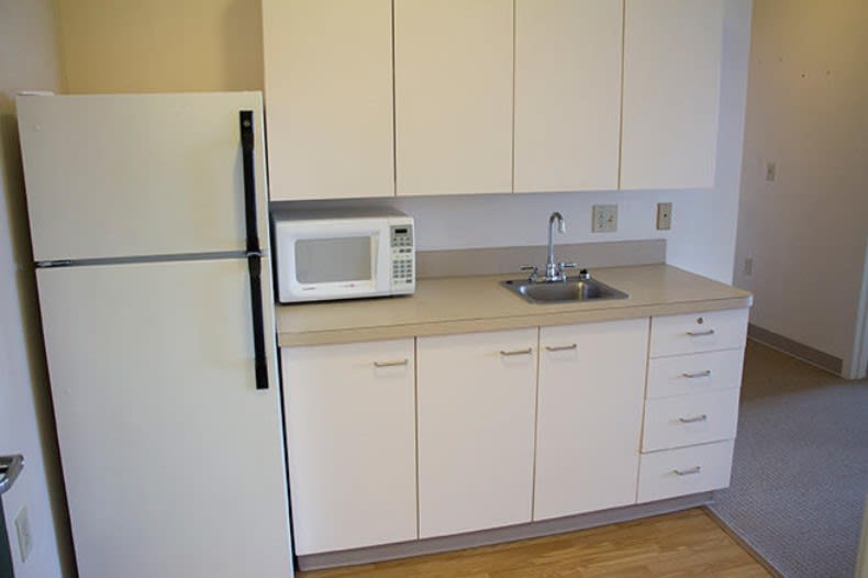 A small kitchen area with a refrigerator, microwave, sink, and cabinets.