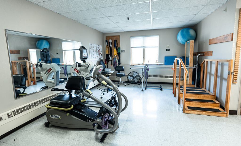 A well-lit fitness room equipped with various exercise machines and rehabilitation equipment.