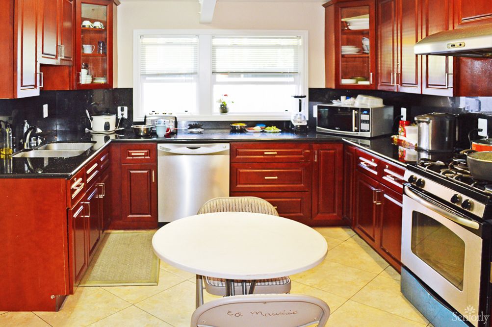 A modern kitchen with wooden cabinets and stainless steel appliances, featuring a small round dining table.