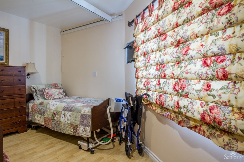 A cozy room featuring a single hospital bed with floral bedding, a matching floral curtain, and a wheelchair.