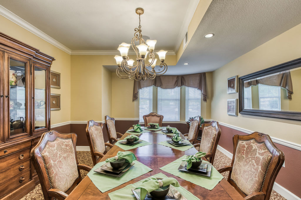 Elegant dining room featuring a large table set for dinner, with a chandelier overhead and large windows adorned with curtains.