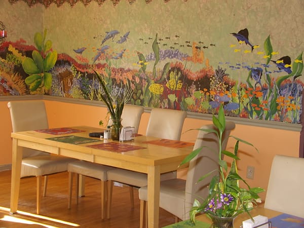 A colorful dining room featuring a vibrant wall mural with plants and a wooden table set.