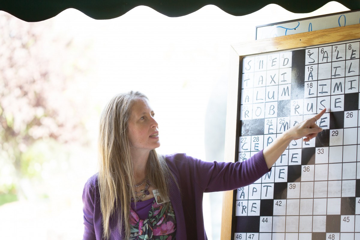 A woman points to a large crossword puzzle on a board, possibly teaching or explaining something.