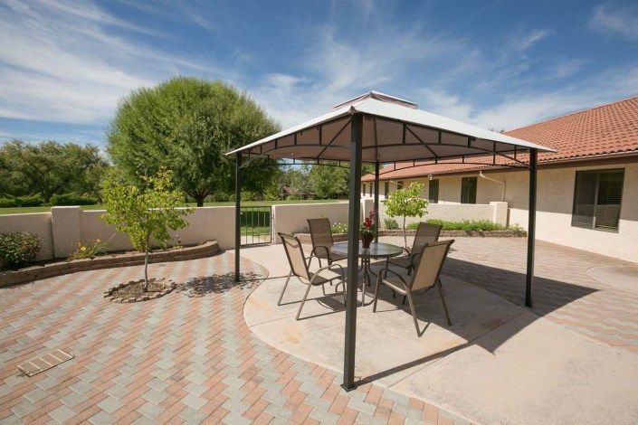 A serene backyard patio featuring a gazebo with outdoor furniture, surrounded by lush landscaping.