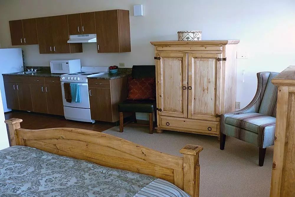 A cozy studio apartment with a combined kitchen and bedroom area featuring wooden furniture.