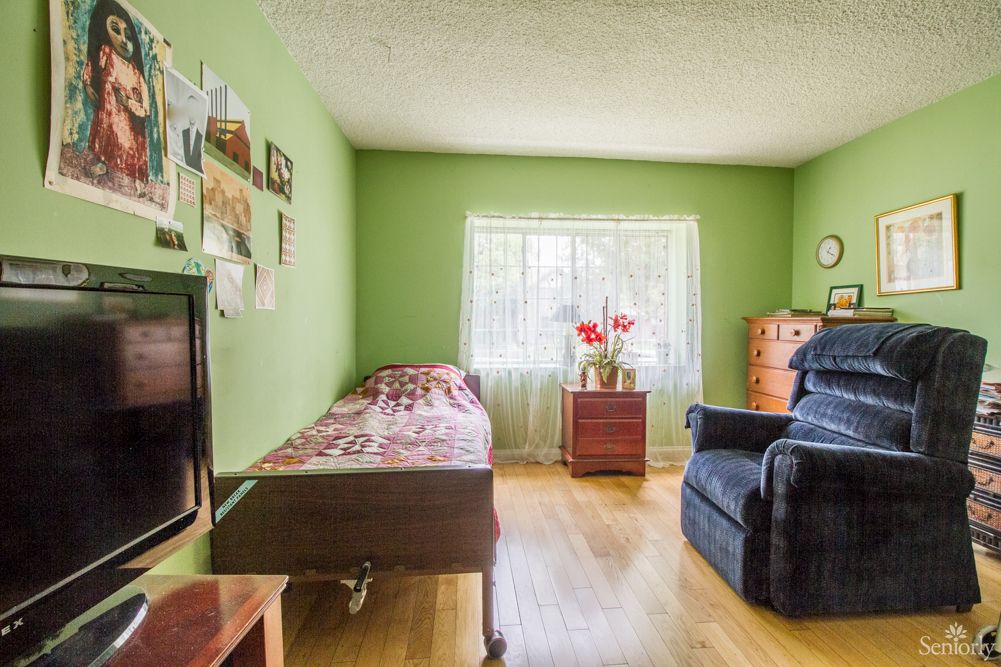 A cozy bedroom with green walls, featuring a single bed, armchair, and window letting in natural light.