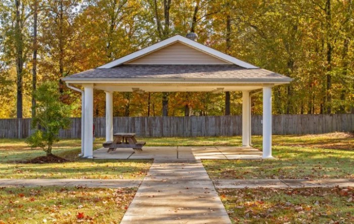 A small pavilion with a picnic table in an autumn park setting.