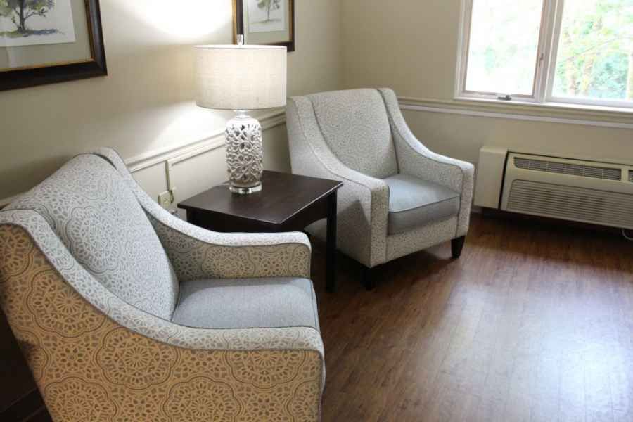 A cozy living room with two armchairs, a side table, and a lamp by the window.