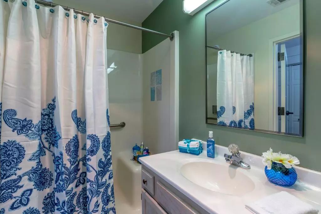 A bathroom with a white and blue themed decor, featuring a shower curtain, sink, and mirror.