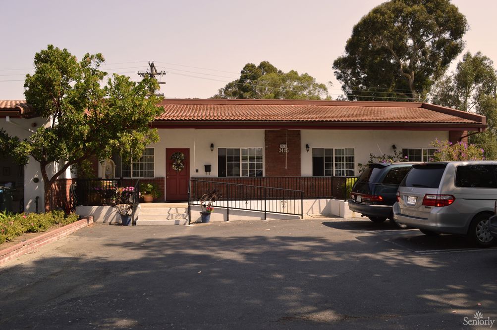 A small one-story building with a parking lot and cars in front, surrounded by trees.