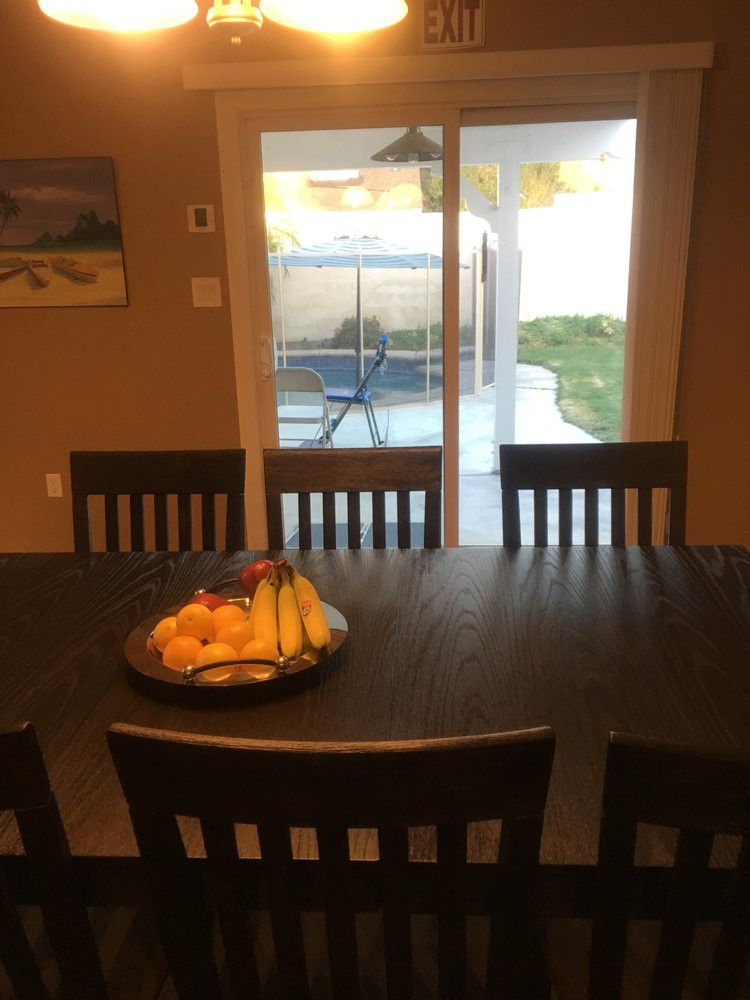 A dining room table with a fruit bowl, facing a sliding glass door in a cozy home setting.